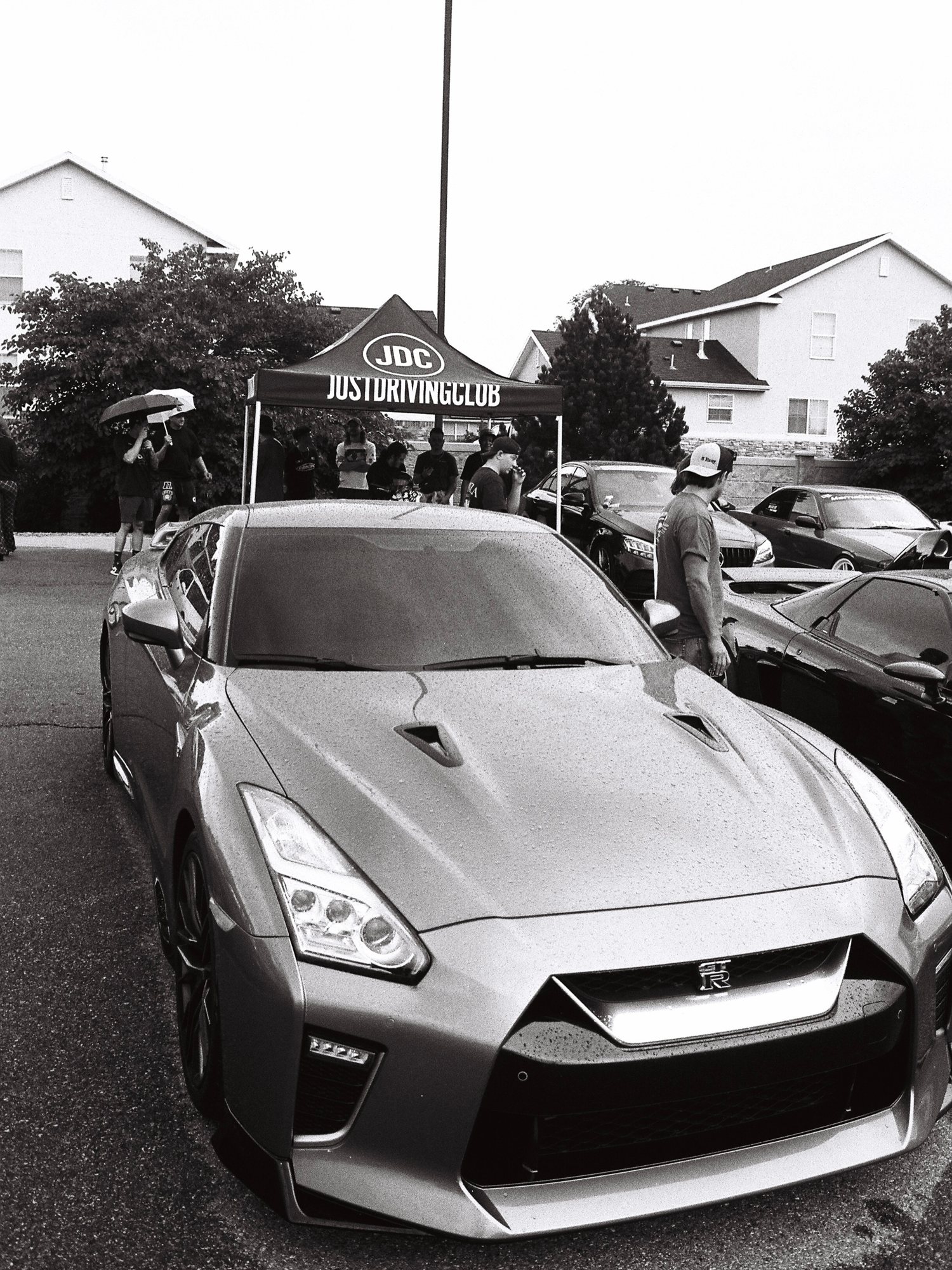 Black and white film photo of a Nissan GT-R in front of the JDC tent