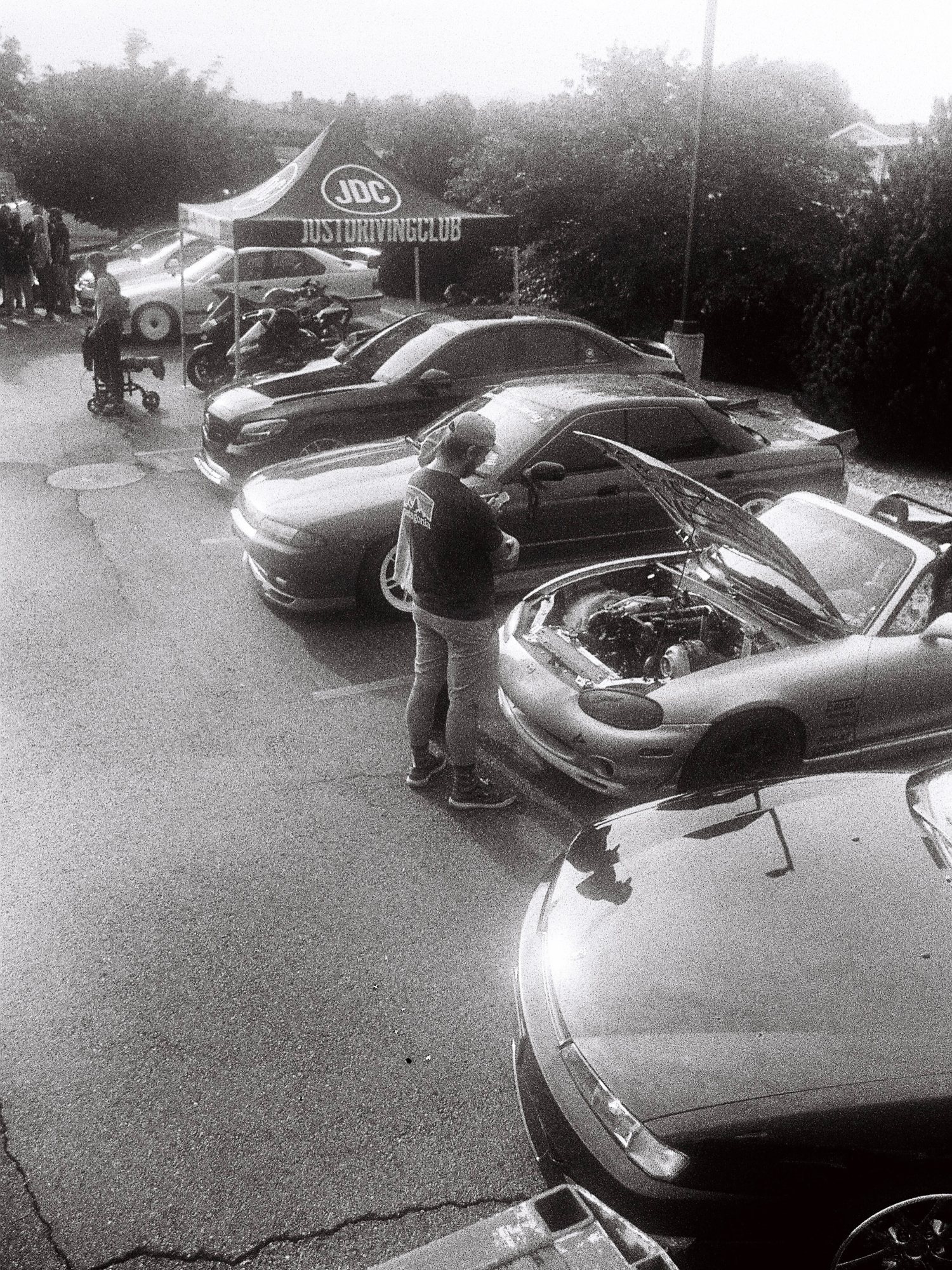 Black and white film photo of a row of cars and the JDC tent